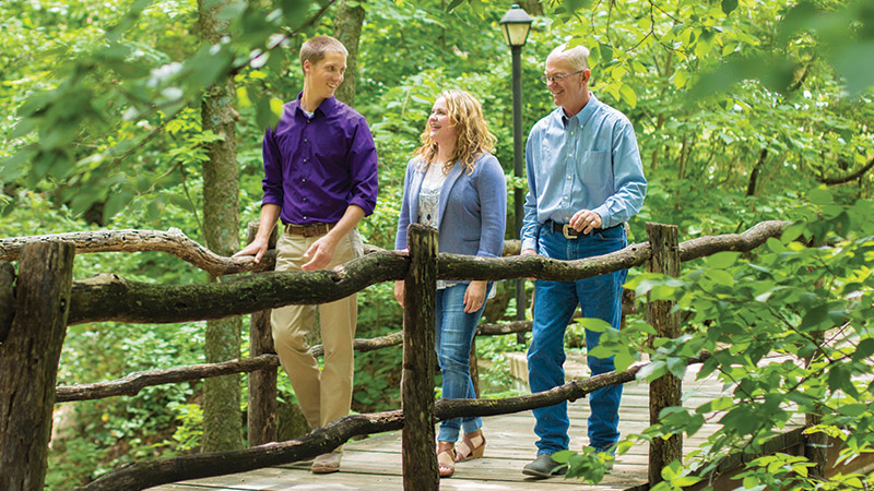 Photo of three people crossing a bridge in nature